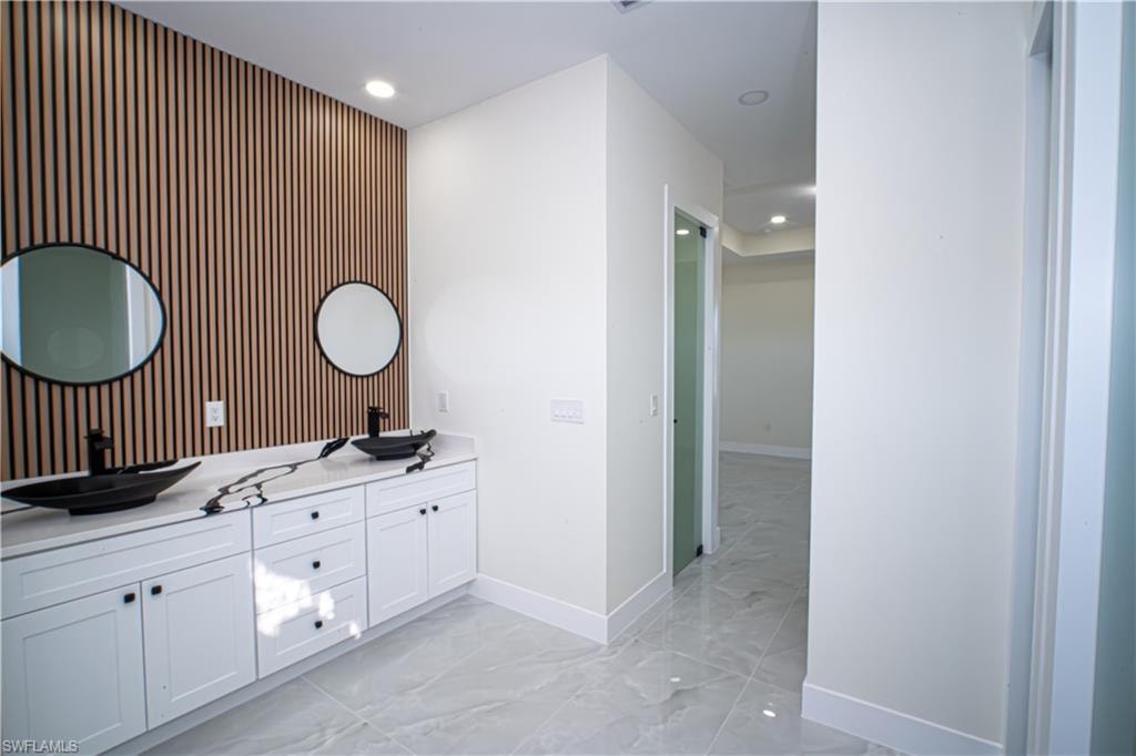 Full bath featuring an accent wall, double vanity, recessed lighting, and light marble finish floors