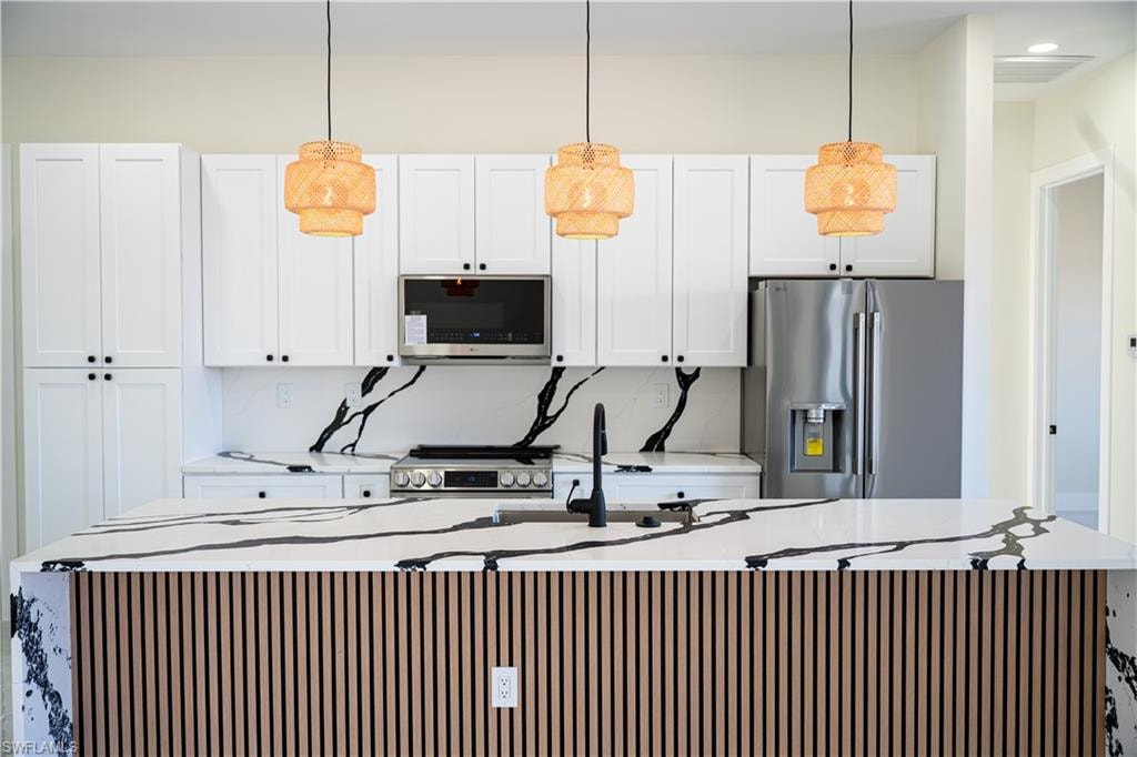 Kitchen featuring light stone counters, a large island with sink, stainless steel appliances, and white cabinets
