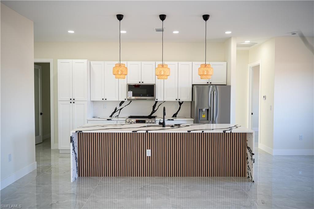 Kitchen featuring a large island, white cabinetry, stainless steel appliances, and hanging light fixtures