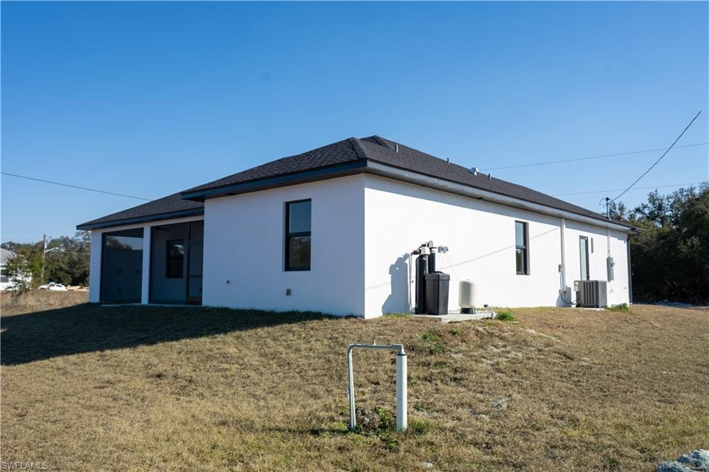 View of property exterior with a yard, stucco siding, and roof with shingles