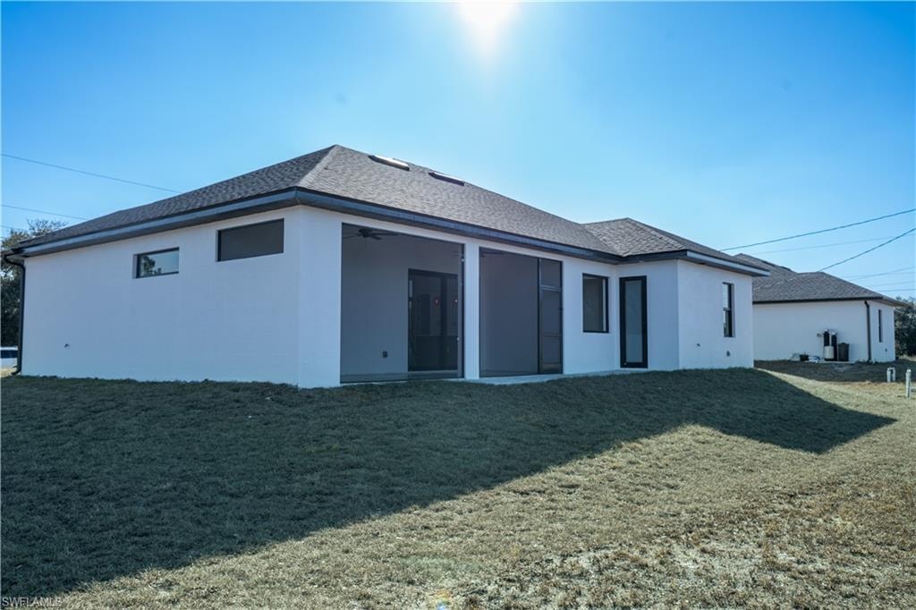 Back of property with a yard, stucco siding, a shingled roof, and a sunroom