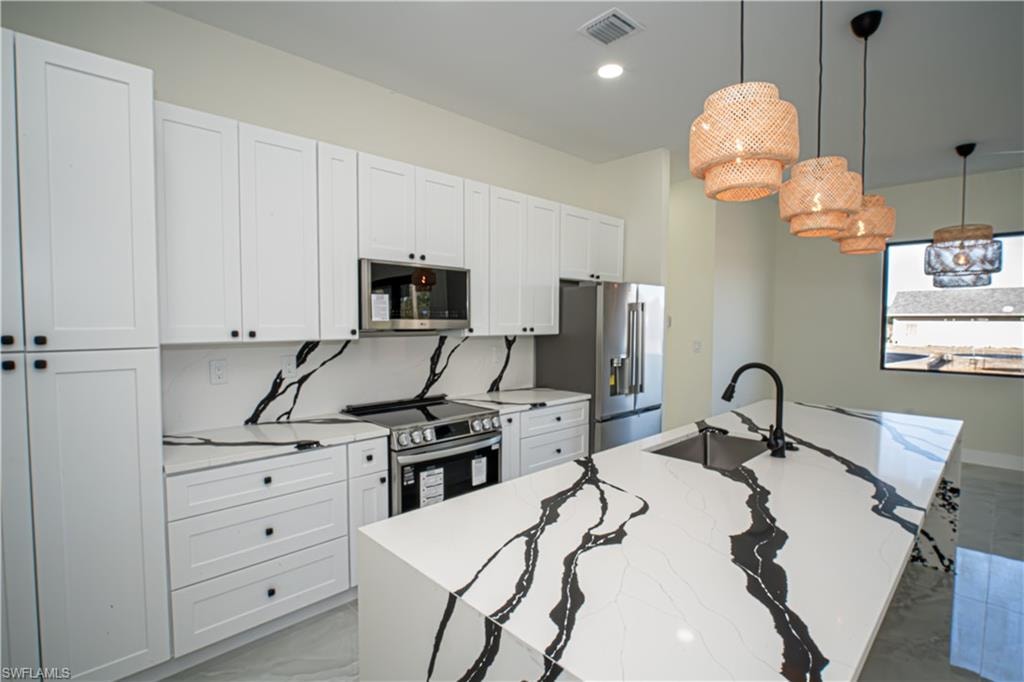 Kitchen featuring a kitchen island with sink, hanging light fixtures, white cabinetry, stainless steel appliances, and light stone counters