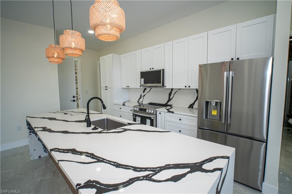 Kitchen with stainless steel appliances, pendant lighting, white cabinetry, an island with sink, and light stone countertops