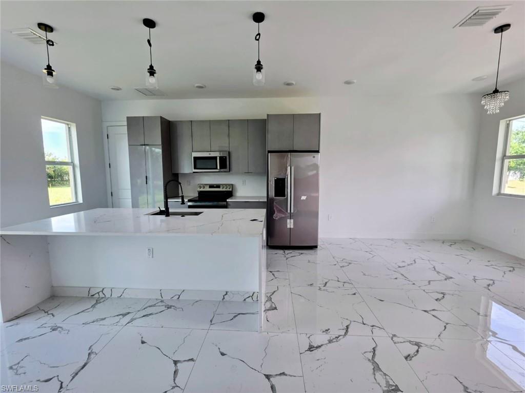 Kitchen with plenty of natural light, pendant lighting, stainless steel appliances, and light stone counters