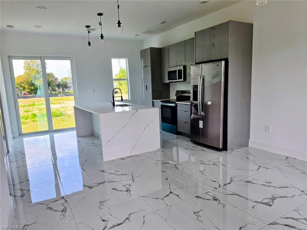 Kitchen featuring stainless steel appliances, a center island with sink, modern cabinets, light stone counters, and hanging light fixtures