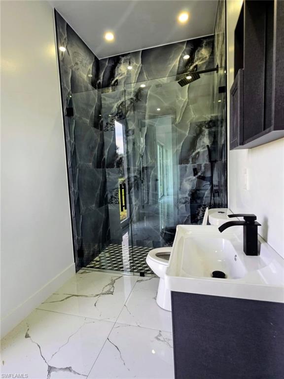 Bathroom featuring vanity, a marble finish shower, light marble finish floors, and recessed lighting