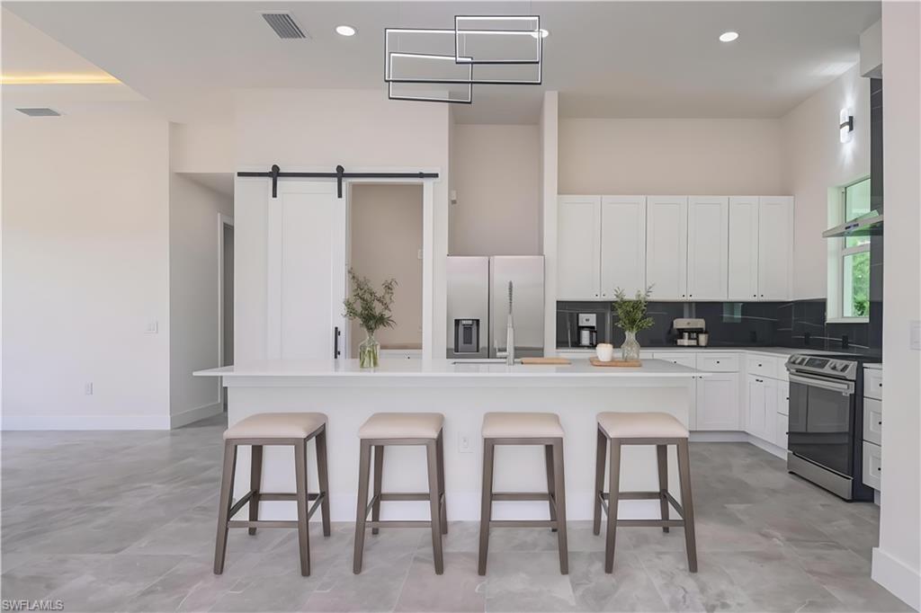 Kitchen featuring a kitchen breakfast bar, an island with sink, stainless steel appliances, and white cabinetry