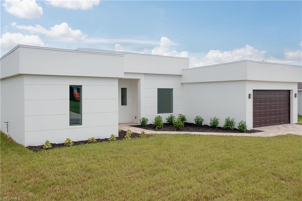View of front of property featuring a front yard, stucco siding, driveway, and a garage