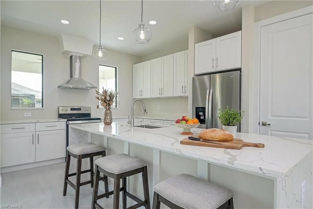 Kitchen featuring light stone counters, pendant lighting, stainless steel appliances, and white cabinets