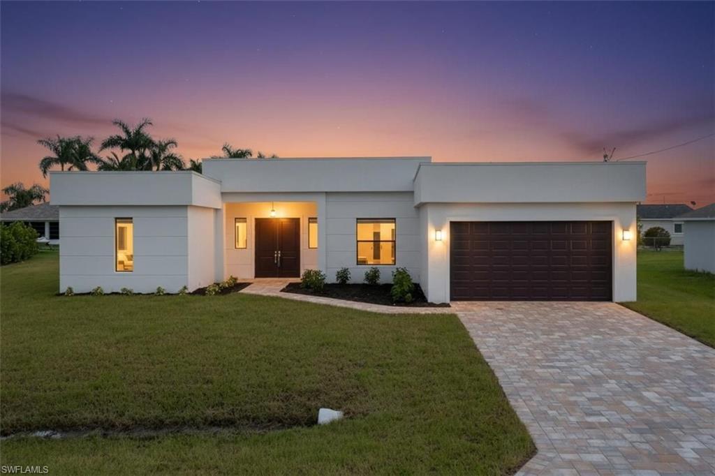 Modern home with a front lawn, decorative driveway, a garage, and stucco siding