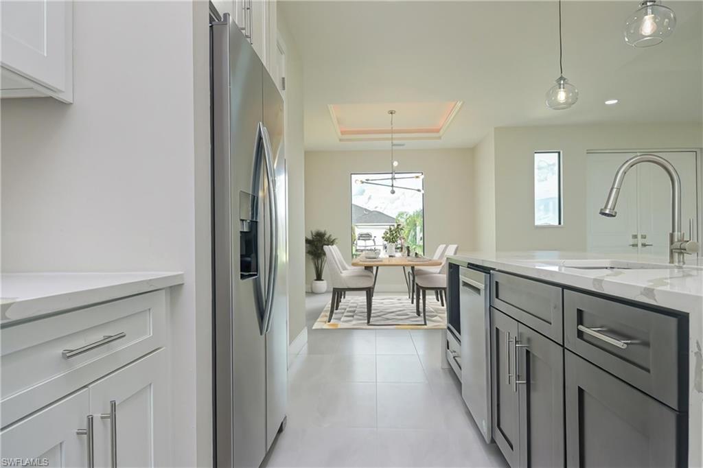 Kitchen with light stone countertops, hanging light fixtures, a tray ceiling, stainless steel appliances, and white cabinetry