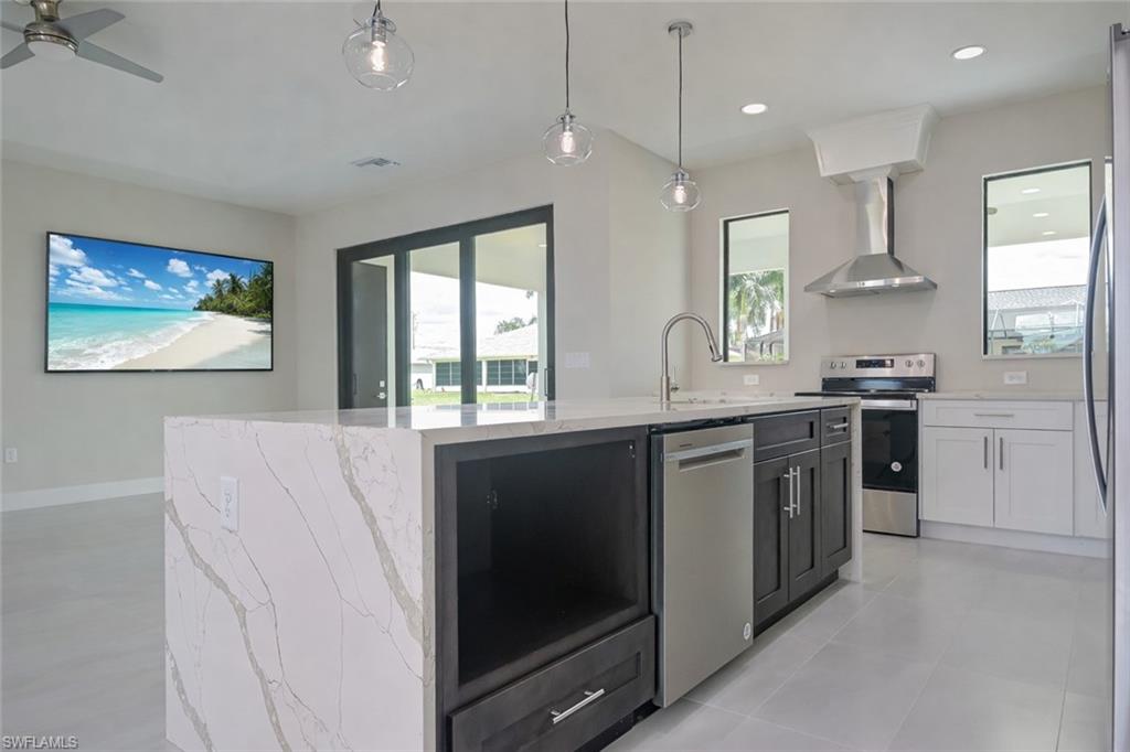 Kitchen with hanging light fixtures, an island with sink, light stone countertops, stainless steel appliances, and a ceiling fan
