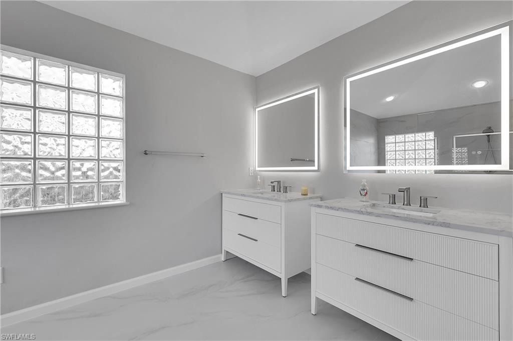 Bathroom with two vanities, walk in shower, comfort height toilet and light marble finish flooring