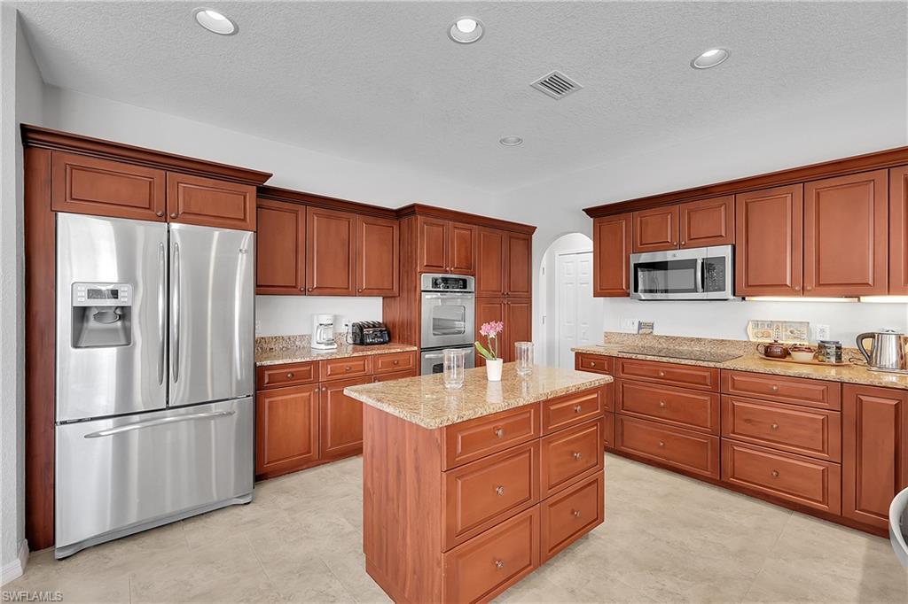 Kitchen with stainless steel appliances, arched walkways, light stone counters, wood finish cabinets, and a kitchen island