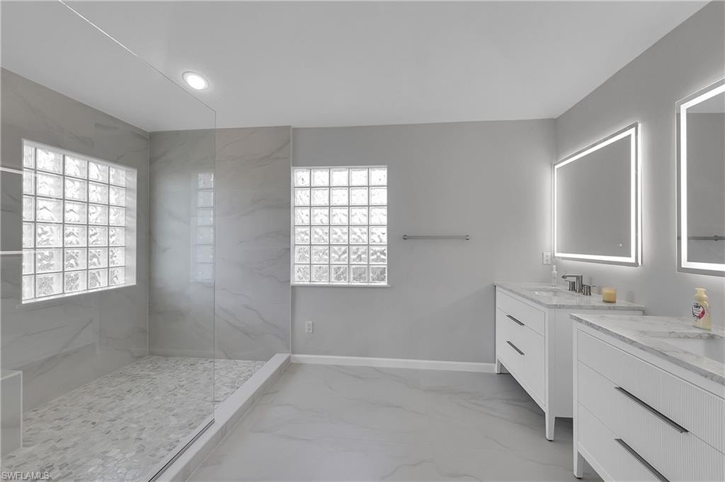 Brand new bathroom featuring a marble finish shower, linear drain, two vanities, recessed lighting, and light marble finish floors