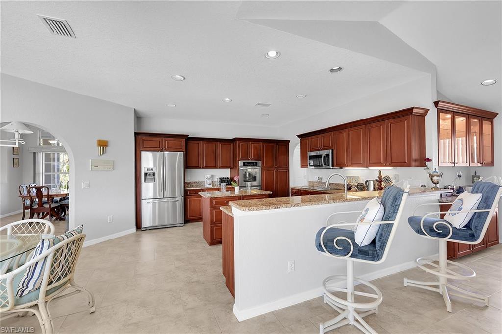 Kitchen featuring a breakfast bar, arched walkways, stainless steel appliances, a peninsula, and light stone counters