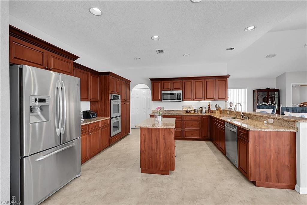 Kitchen featuring stainless steel appliances, a peninsula, arched walkways, light stone countertops, pullout drawers in cabinets, turntables in corner cabinet and recessed lighting