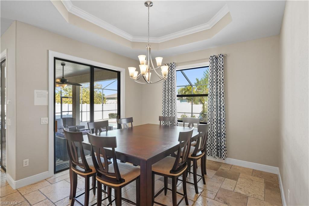 Dining room with stone tile floors, ornamental molding, a raised ceiling, ceiling fan, and a chandelier