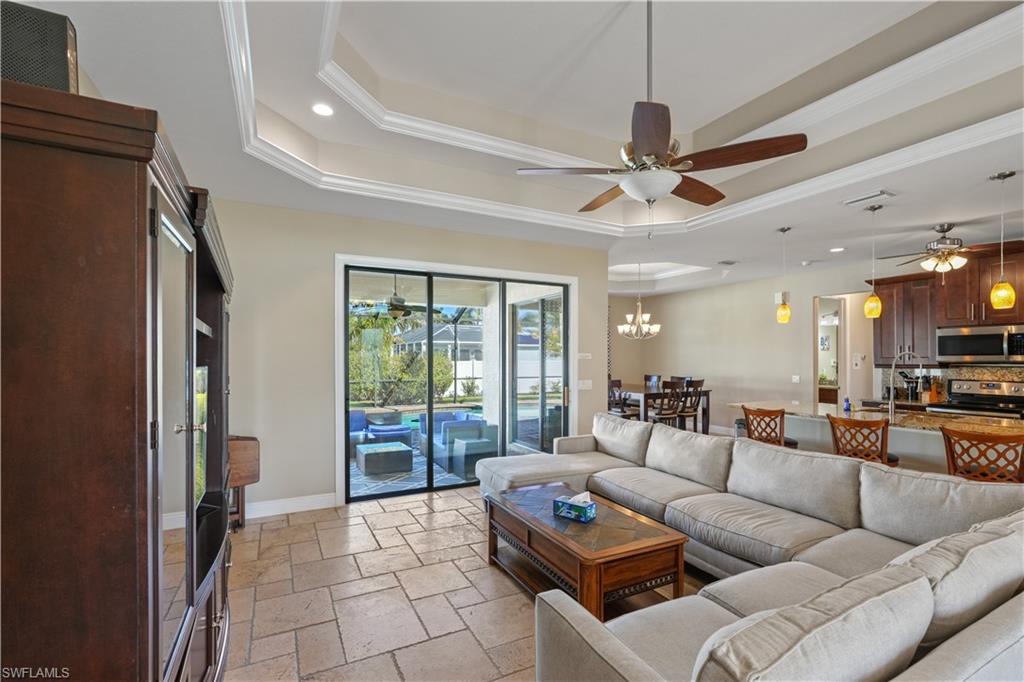 Living room featuring stone tile flooring, ornamental molding, a tray ceiling, ceiling fan, and hanging lights