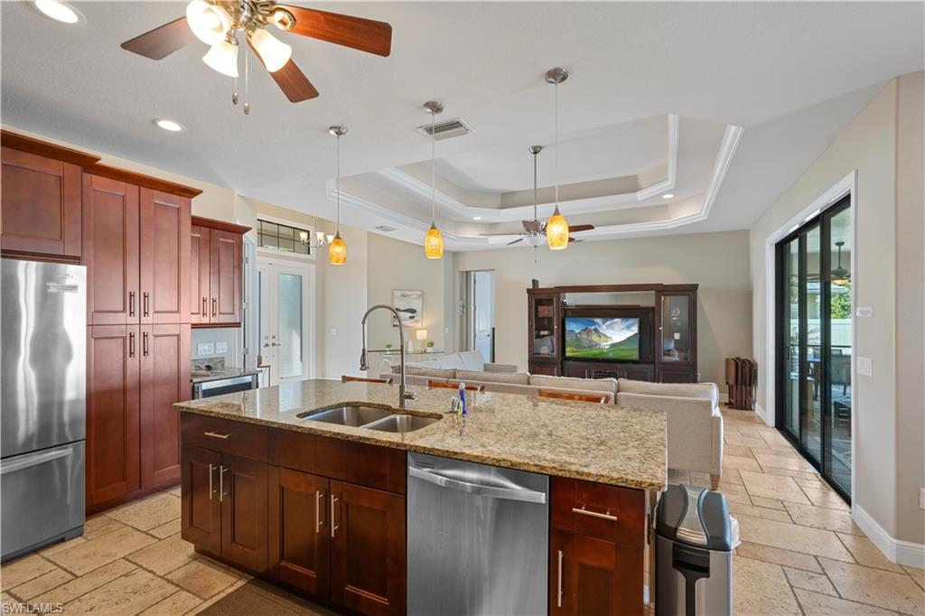 Kitchen with a ceiling fan, stone tile floors, stainless steel appliances, pendant lighting, and a tray ceiling