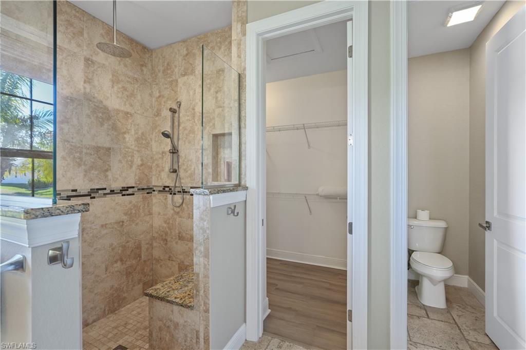 Bathroom featuring a walk in shower, a spacious closet, and light wood-style floors