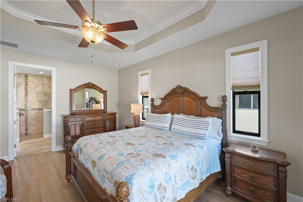 Bedroom featuring wood finished floors, crown molding, ceiling fan, connected bathroom, and multiple windows