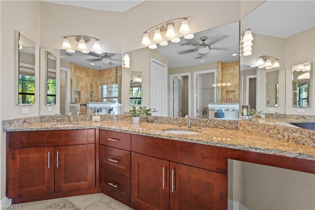 Bathroom featuring double vanity, tiled shower, and ceiling fan