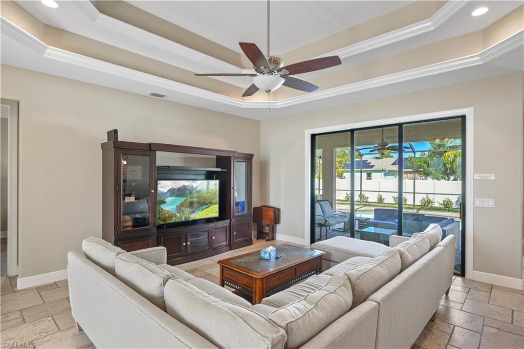 Living room featuring stone tile floors, a ceiling fan, crown molding, and a tray ceiling