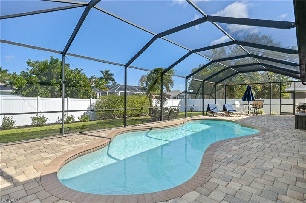 View of pool with a fenced backyard, glass enclosure, a sunroom, and patio surround