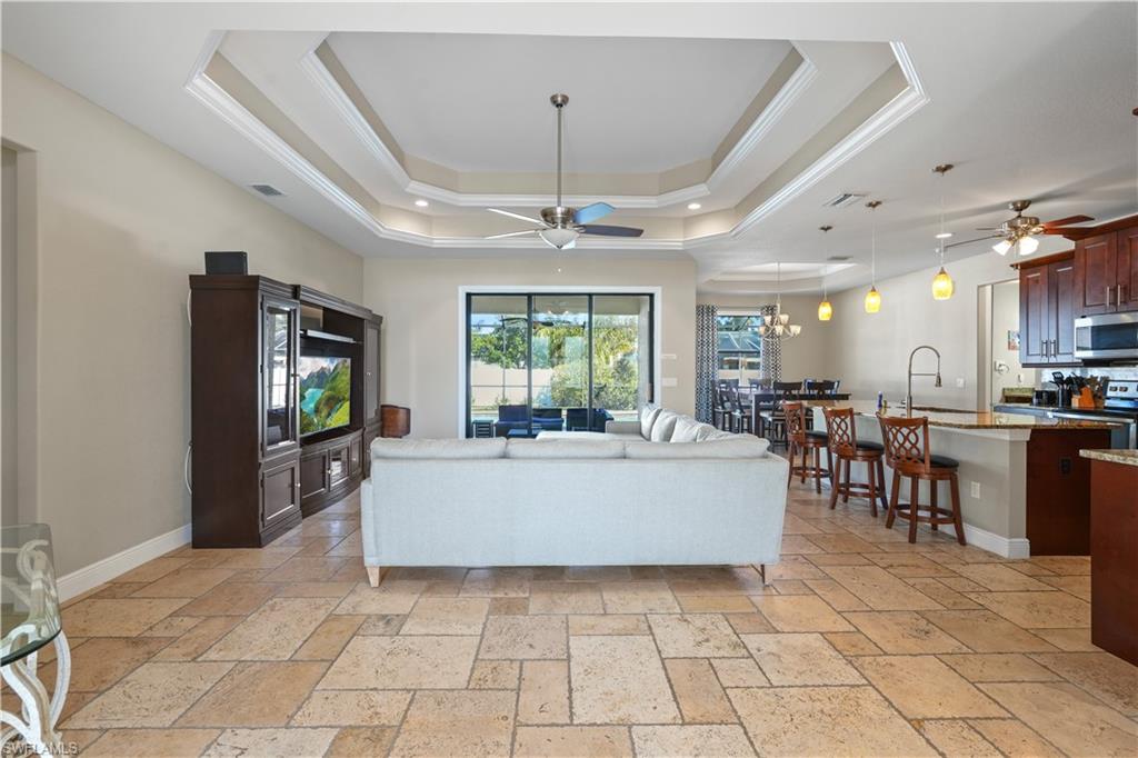 Living area featuring ceiling fan, stone tile floors, crown molding, and a chandelier