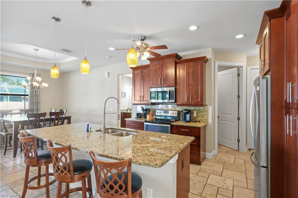 Kitchen featuring stone tile flooring, a breakfast bar, stainless steel appliances, decorative backsplash, and ceiling fan