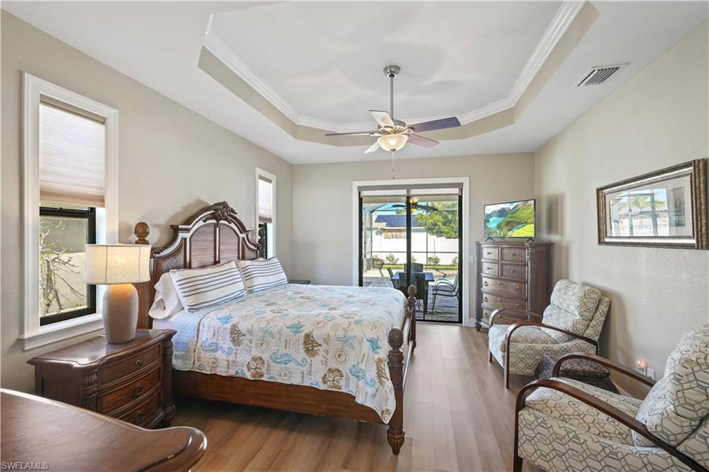 Bedroom with access to exterior, wood finished floors, ceiling fan, a tray ceiling, and ornamental molding