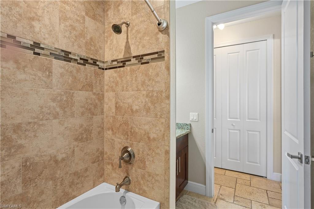 Bathroom featuring stone tile floors, bathing tub / shower combination, vanity, and a closet