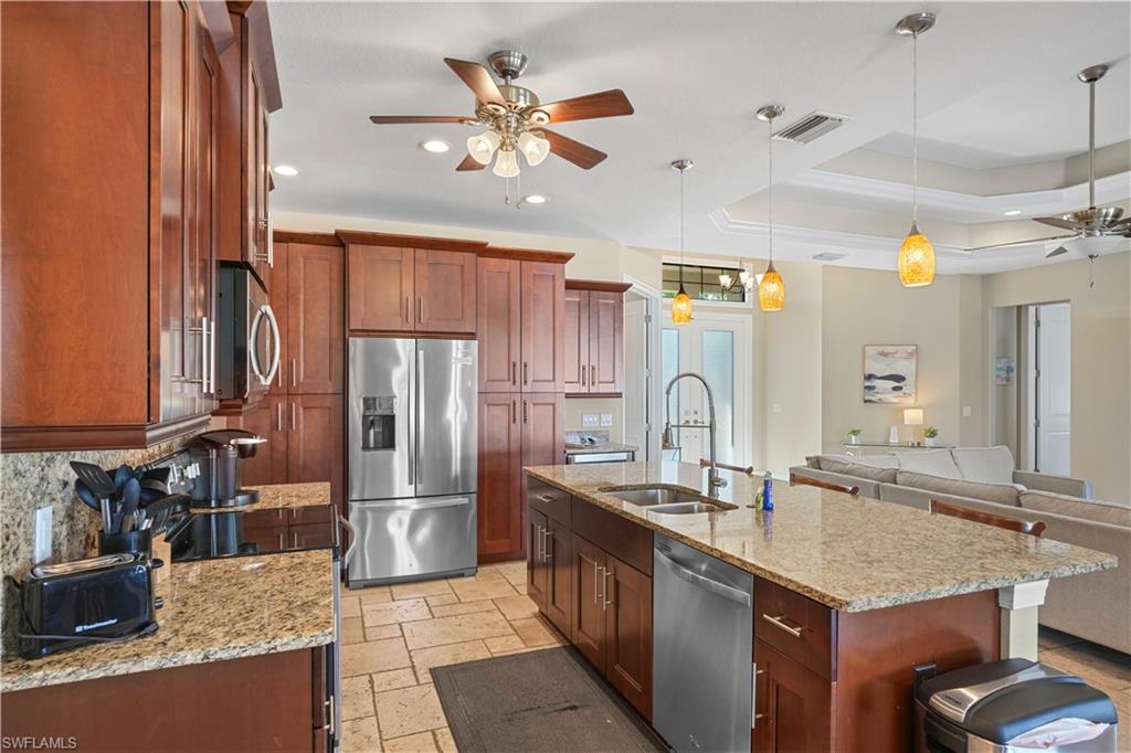 Kitchen with a ceiling fan, light stone counters, stainless steel appliances, stone tile floors, and a raised ceiling