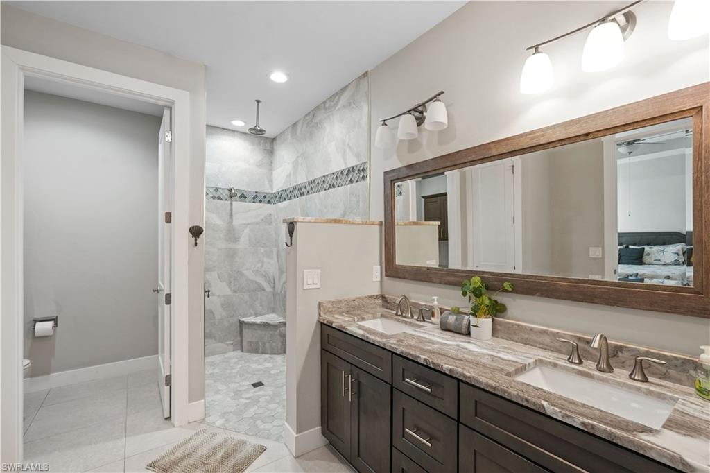 Full bath featuring a walk in shower, double vanity, ensuite bathroom, light tile patterned floors, and recessed lighting