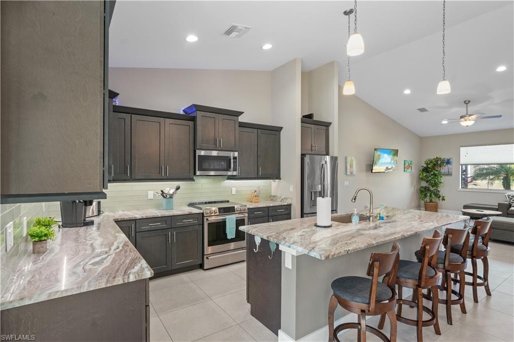 Kitchen with backsplash, stainless steel appliances, an island with sink, a breakfast bar, and light stone countertops