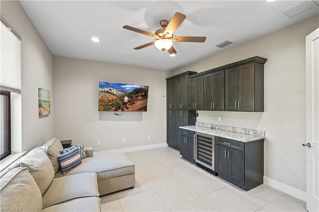 Bar with wine cooler, a ceiling fan, recessed lighting, light stone counters, and dark cabinetry