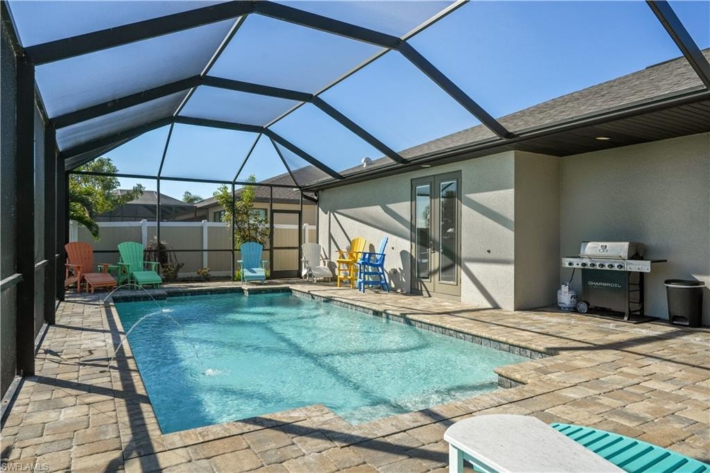 View of pool with patio surround, glass enclosure, a sunroom, and area for grilling