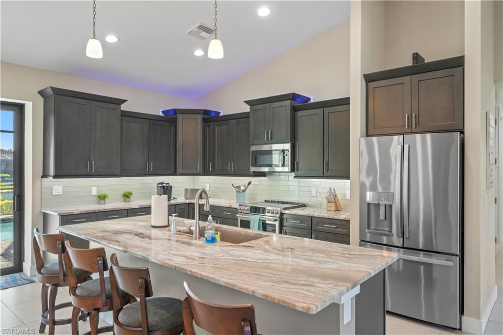 Kitchen featuring stainless steel appliances, light stone countertops, light tile patterned floors, a kitchen island with sink, and lofted ceiling