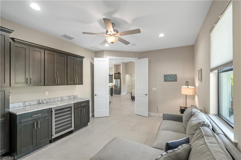 Bar with ceiling fan, beverage cooler, stainless steel fridge, light stone countertops, and recessed lighting