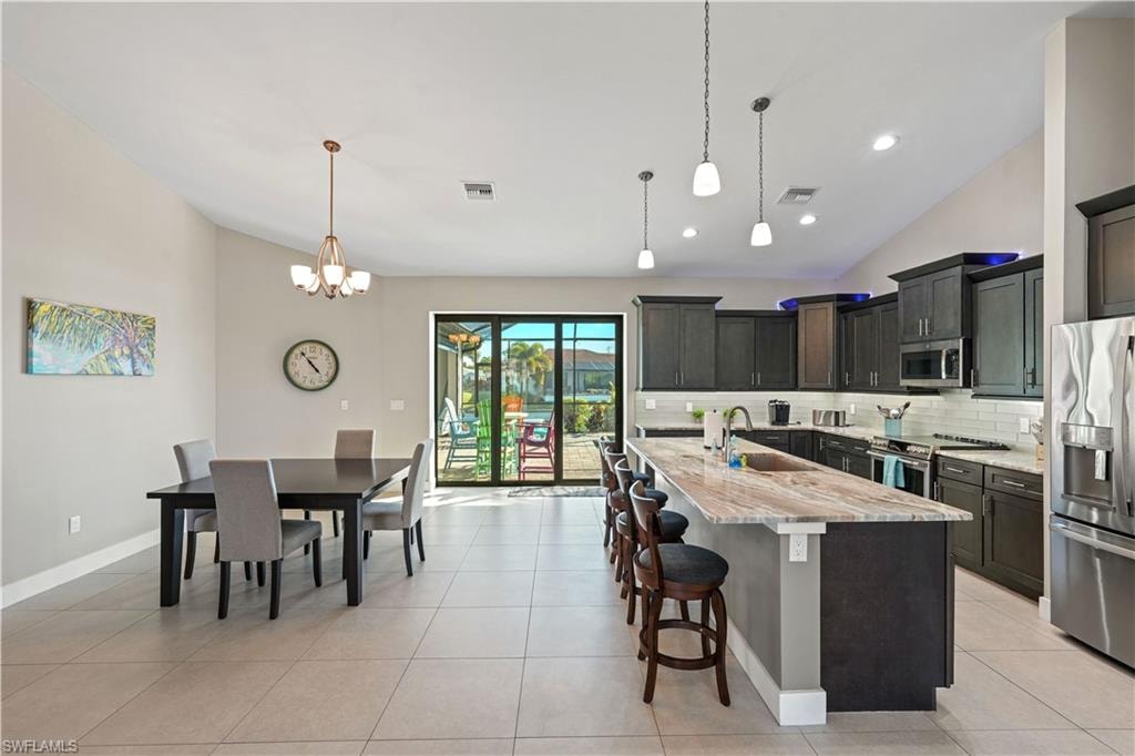 Kitchen featuring lofted ceiling, stainless steel appliances, a kitchen breakfast bar, light stone countertops, and an island with sink