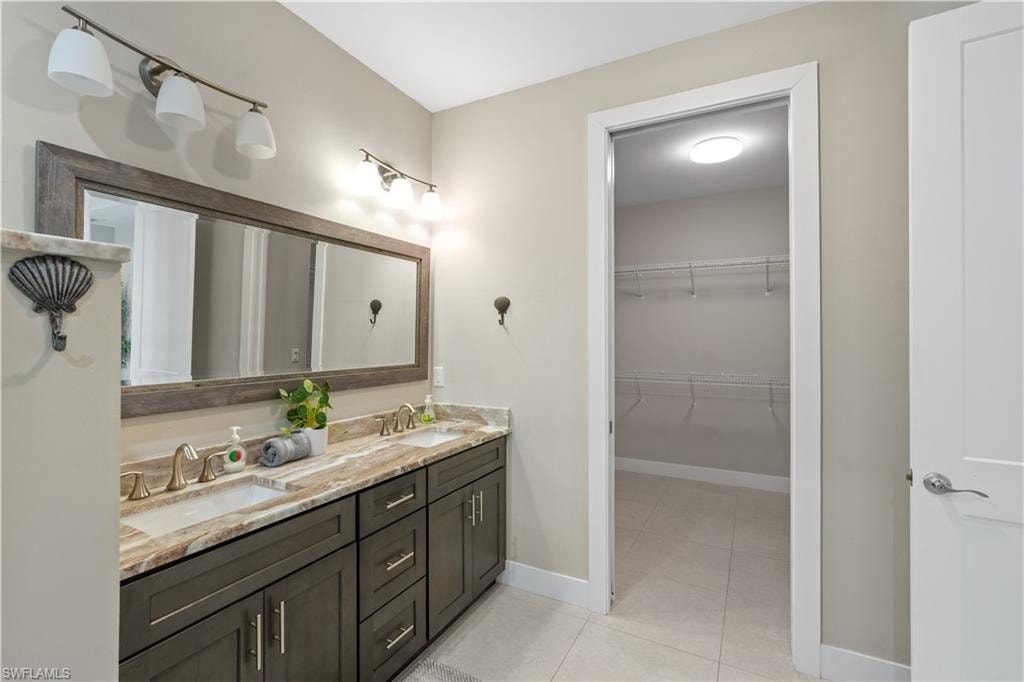 Full bath with double vanity, light tile patterned floors, and a spacious closet