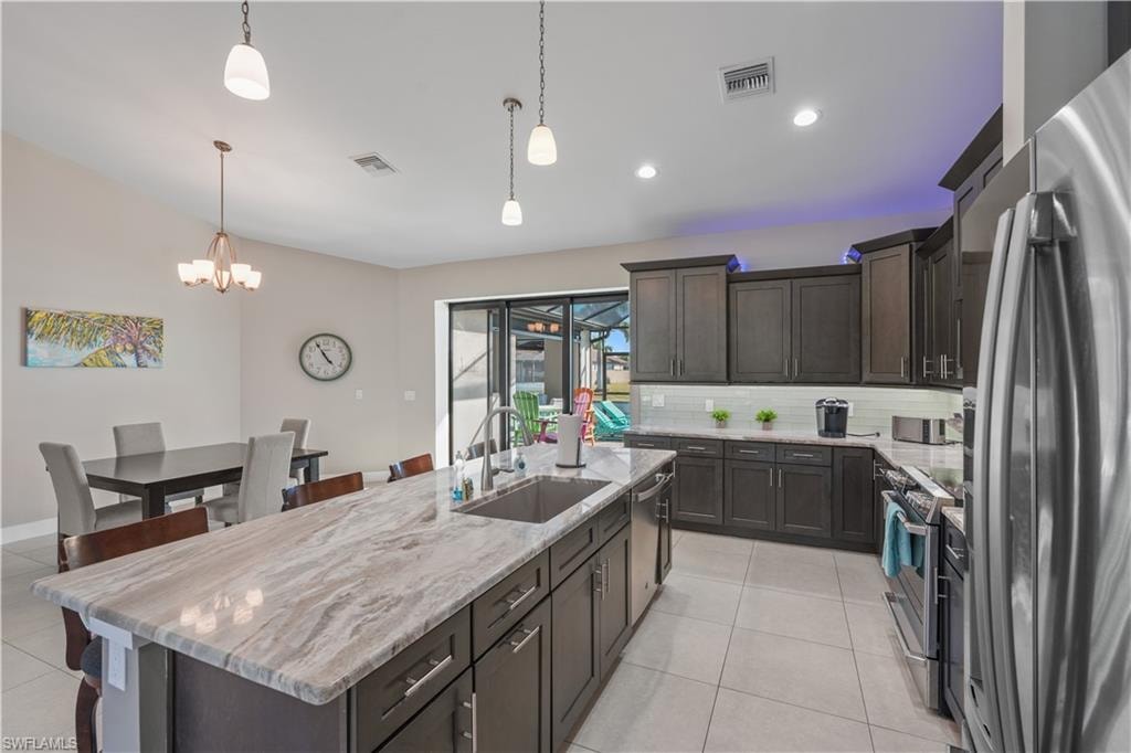 Kitchen featuring stainless steel appliances, dark wood finish cabinetry, a center island with sink, and a kitchen bar