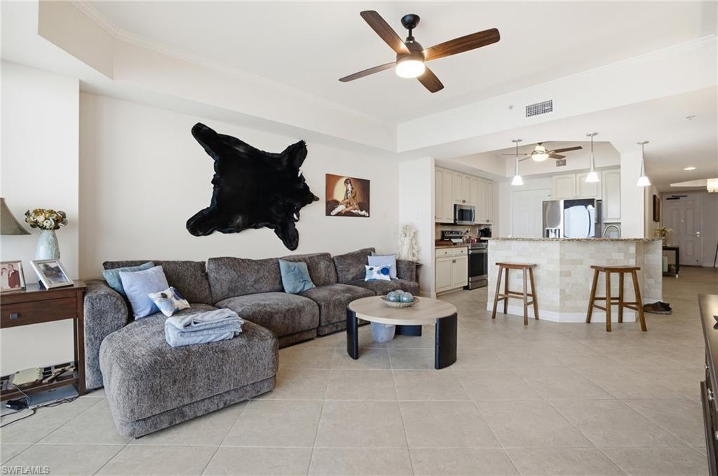 Living room with a raised ceiling, ceiling fan, light tile patterned floors, and crown molding