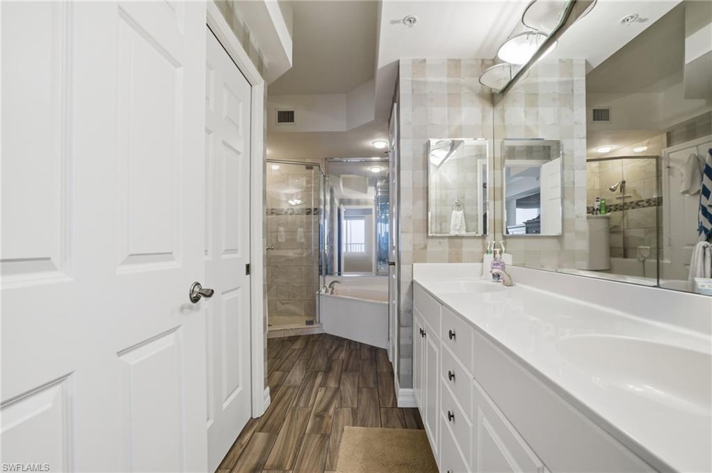 Full bathroom featuring a bath, double vanity, a stall shower, and dark wood-style floors