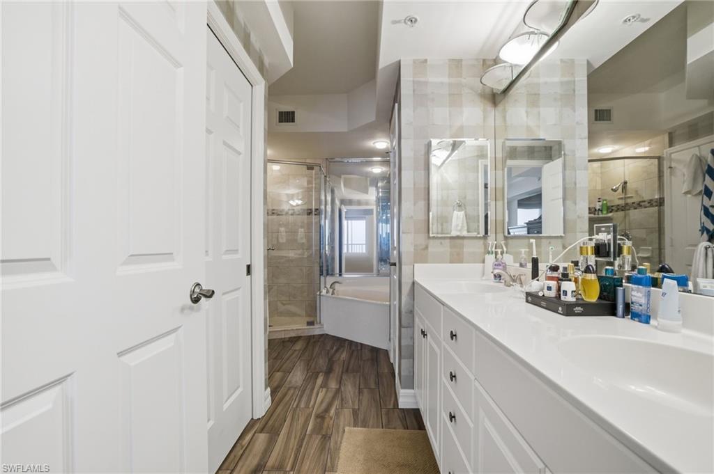 Full bathroom featuring a bath, double vanity, a stall shower, and dark wood-type flooring