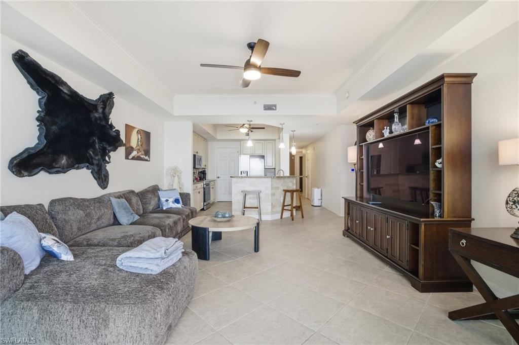 Living area featuring a ceiling fan, a tray ceiling, crown molding, and light tile patterned floors