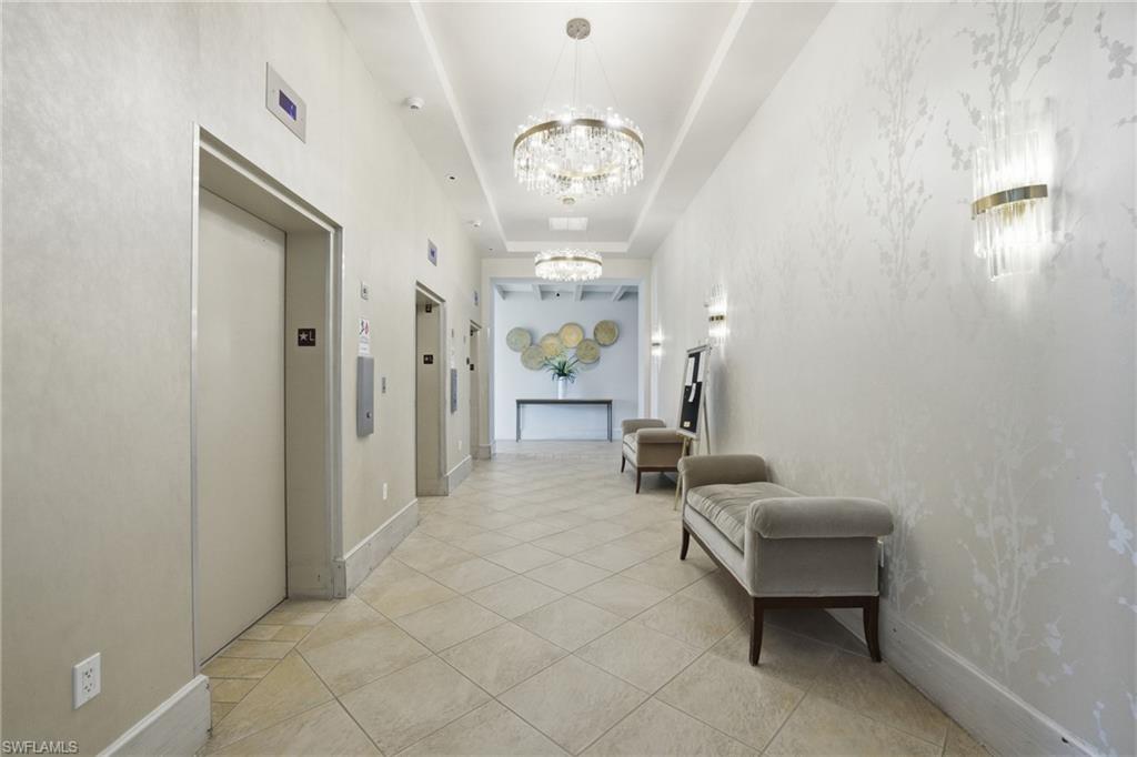 Corridor featuring a raised ceiling, elevator, light tile patterned floors, and a chandelier