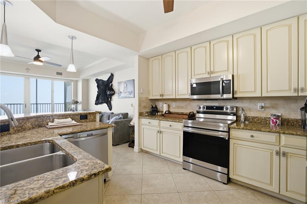 Kitchen featuring cream cabinetry, a ceiling fan, appliances with stainless steel finishes, and dark stone counters