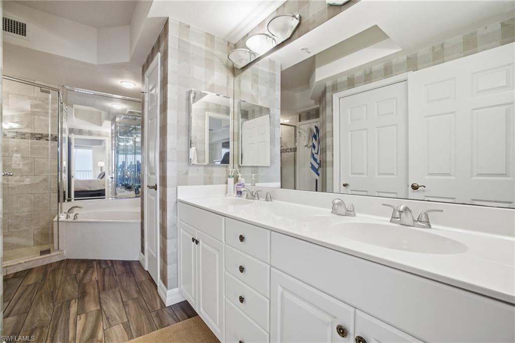 Full bath featuring double vanity, wood finish floors, a bath, and a stall shower